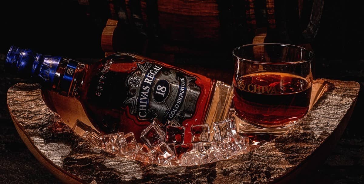 A bottle of Chivas 18-Year-Old and a a tumbler glass in a wood casks tray