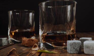 Two glasses of whisky close to a few whisky stones