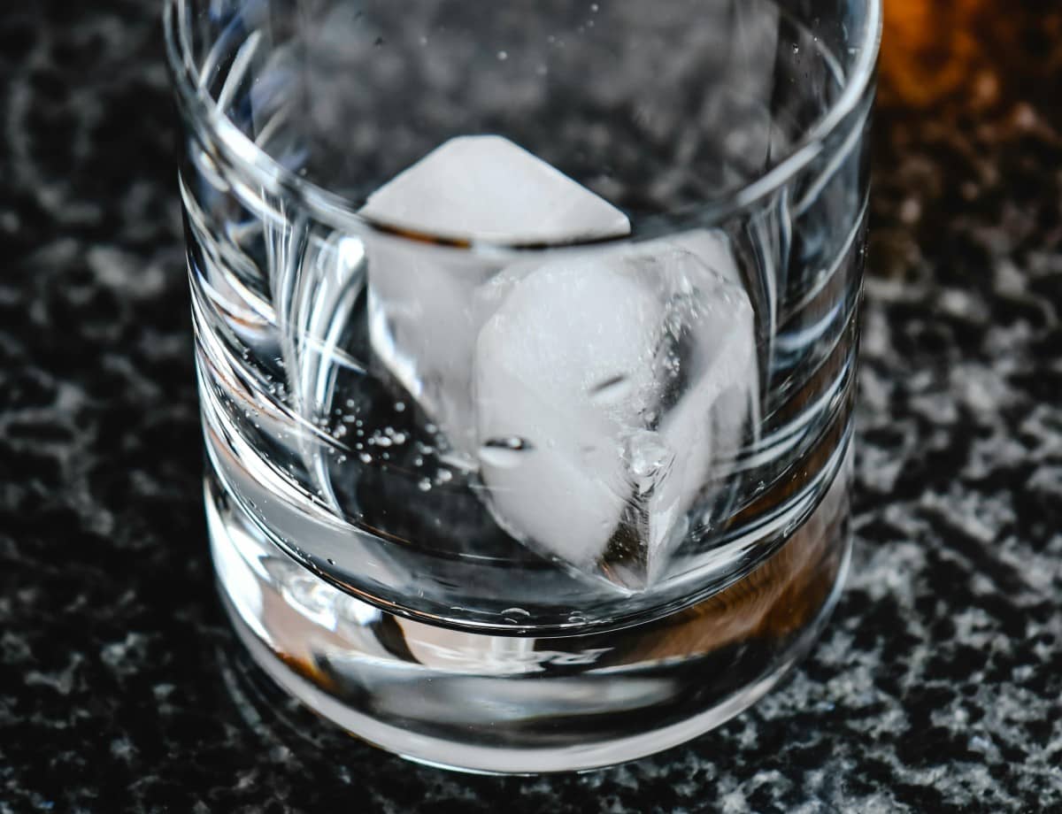 Two ice cubes on a tumbler glass for whisky, on top of a marble table.