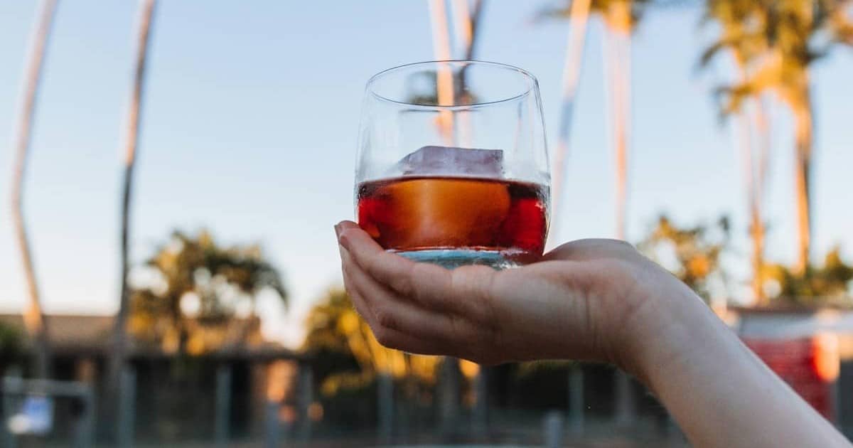 Hand holding a glass of whisky with a big ice cube on it