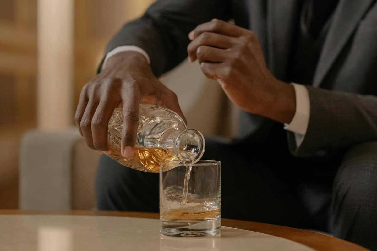 person puring whiskey in a round tumbler glass with ice