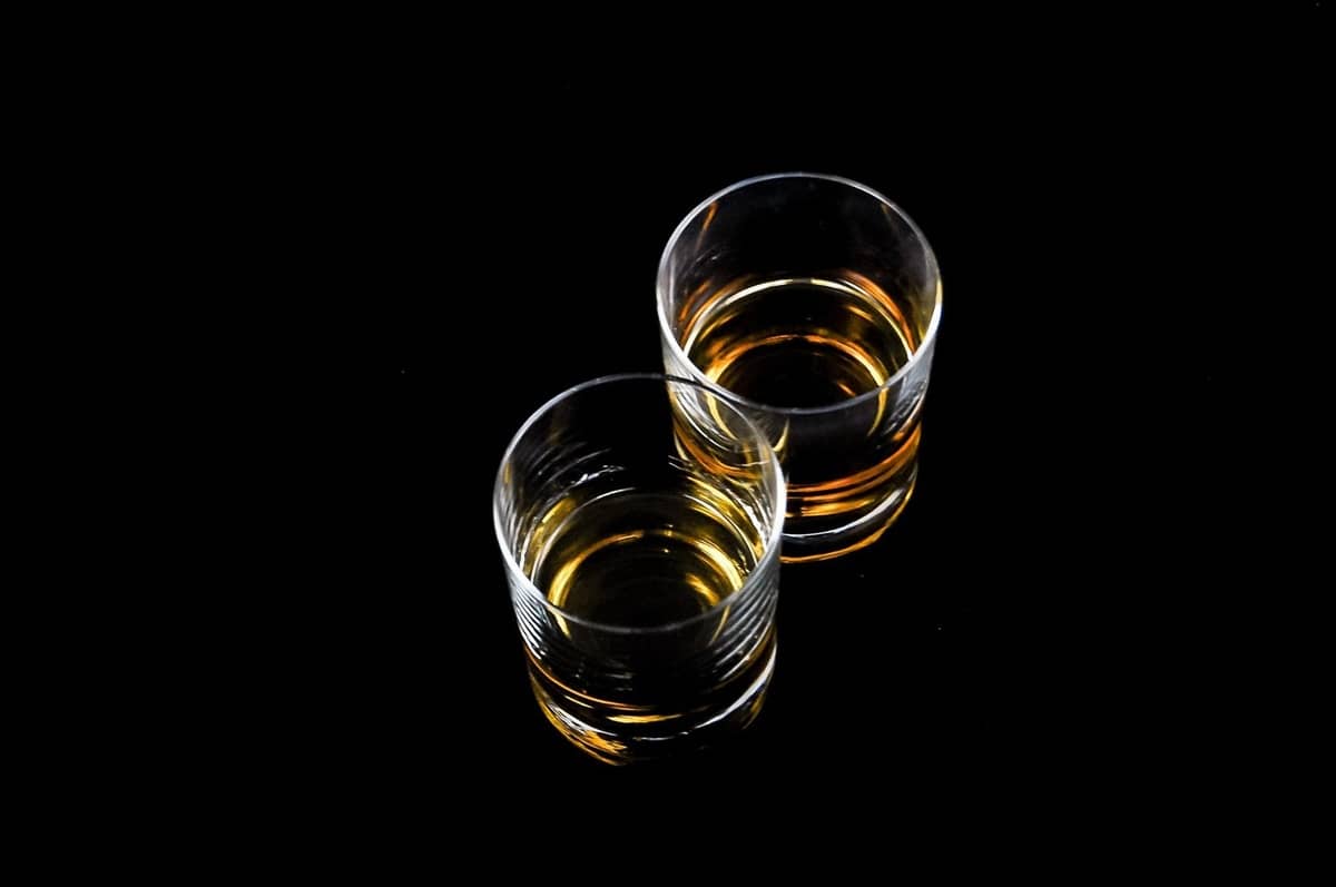 two tumbler glasses with whiskey in a dark background