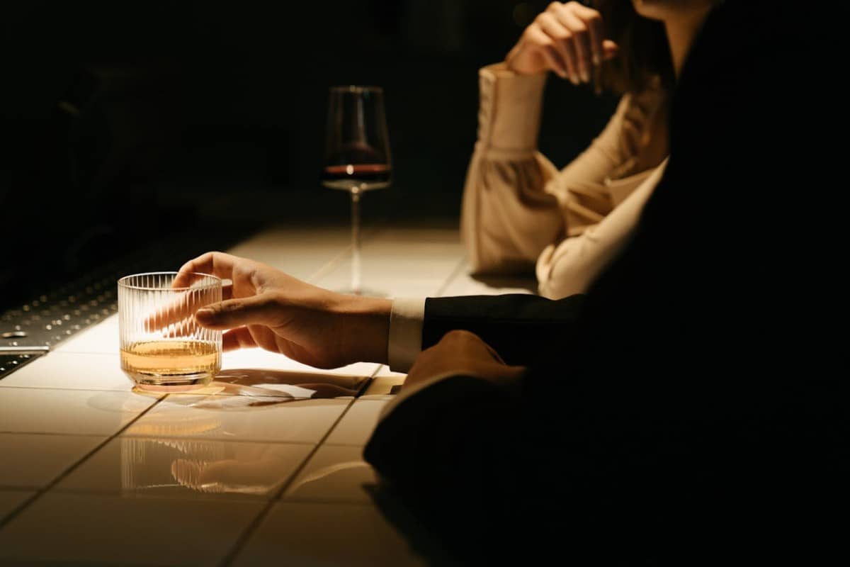 Two people in a bar counter holding a glass of wine and a whiskey tumbler
