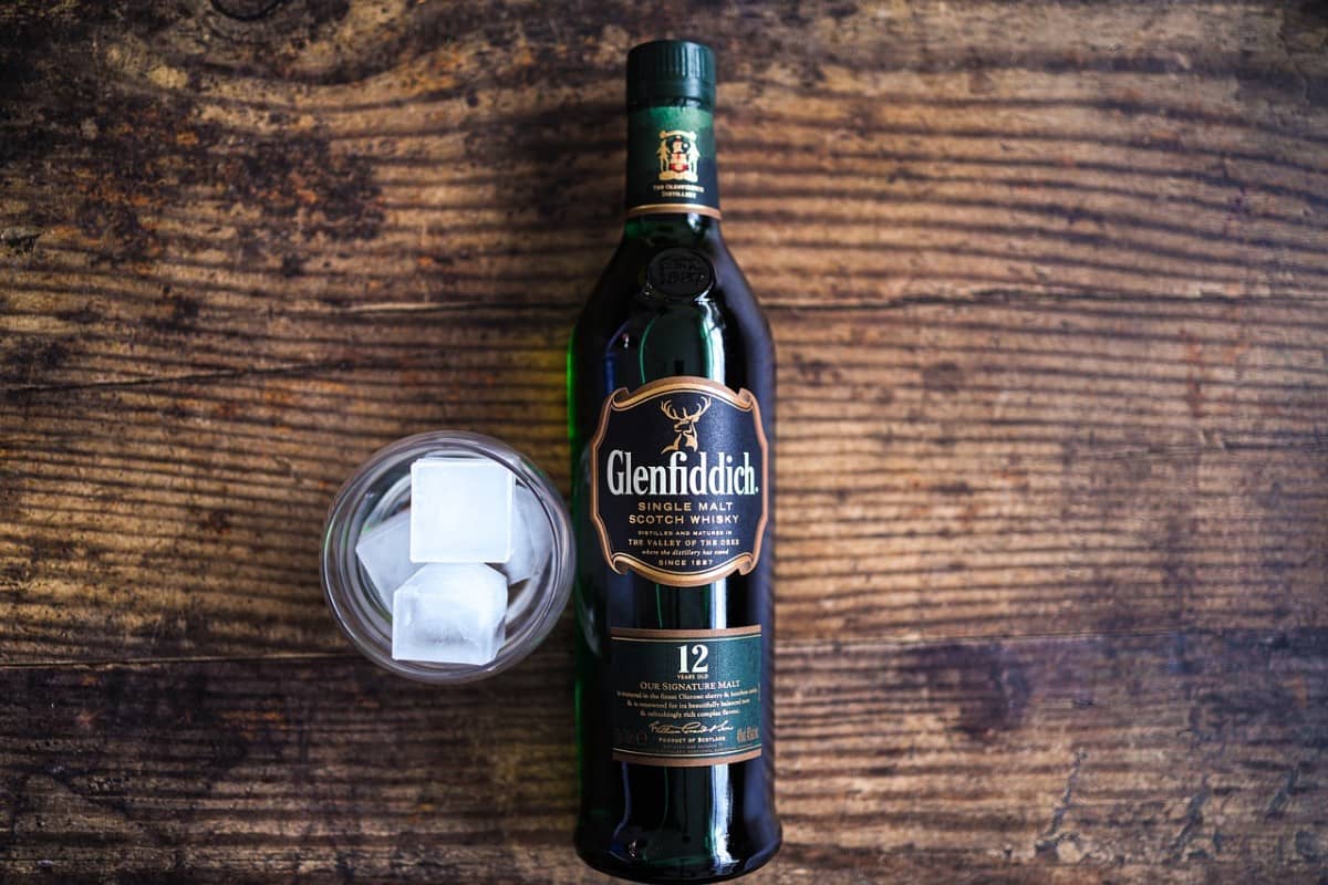 Bottle of Glenfiddich single malt scotch on a wooden table with a glass with ice on its side