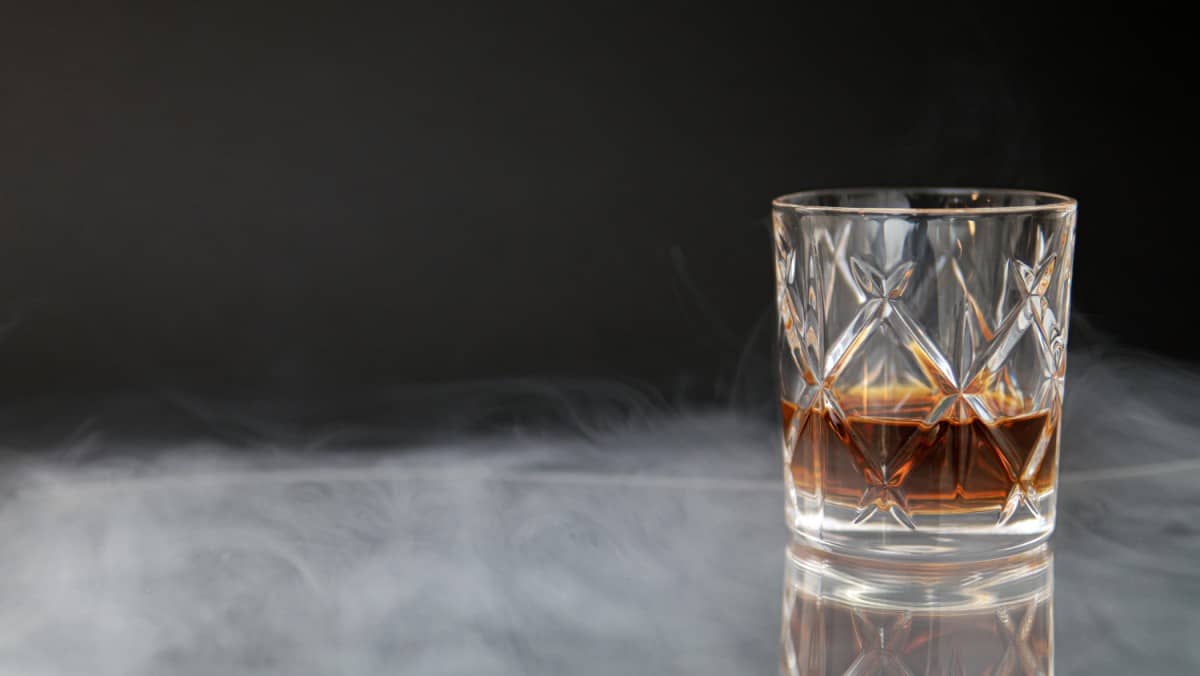 Glass of whiskey surrounded by smoke in a glass table and a black background